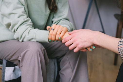 two people siting down facing each other and holding hands